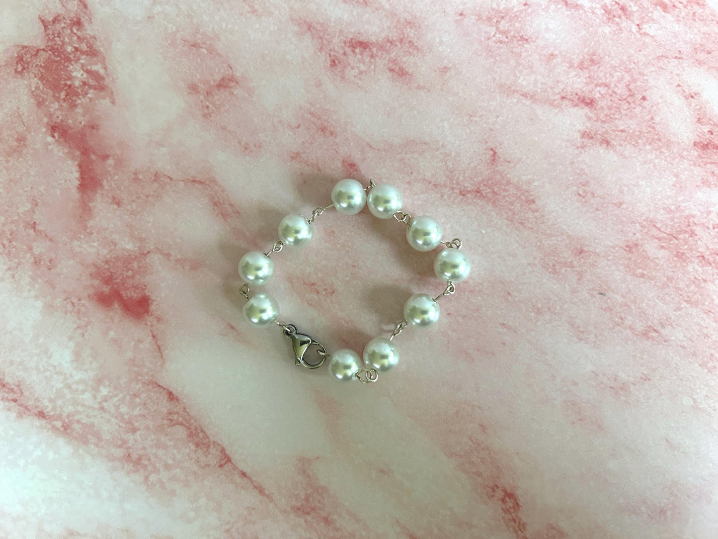 Pearl link bracelet clasped on a pink marble background.