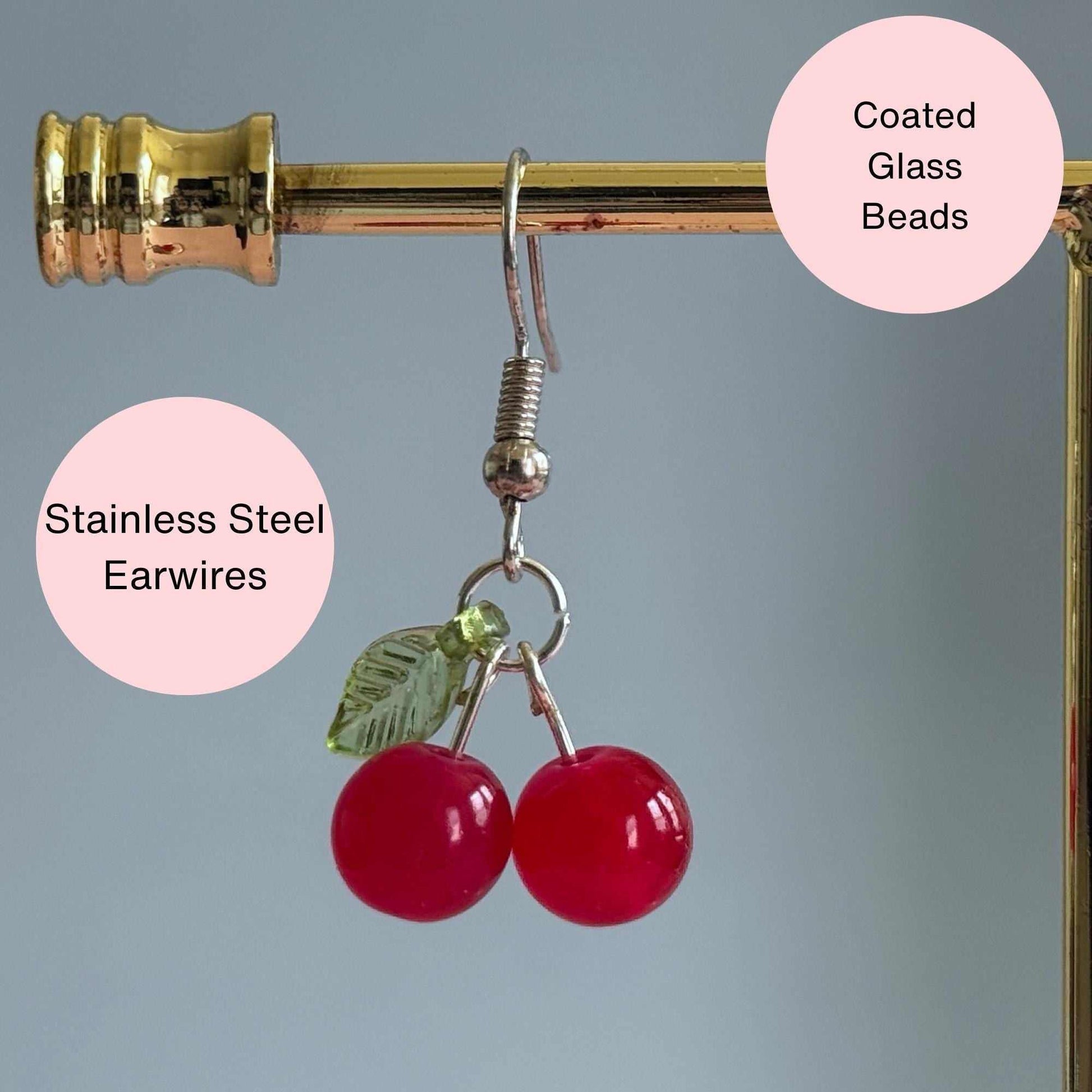 Red cherry earrings on a stand with text explaining that the earrings are coated glass, acrylic, and stainless steel