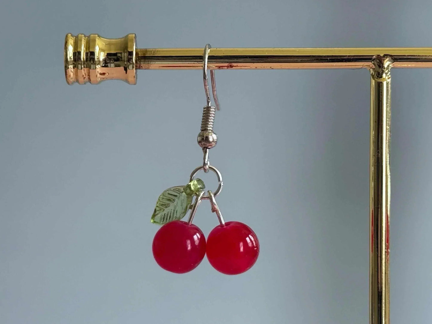 Handmade cherry dangle earrings with red glass beads and a green leaf, perfect for summer.