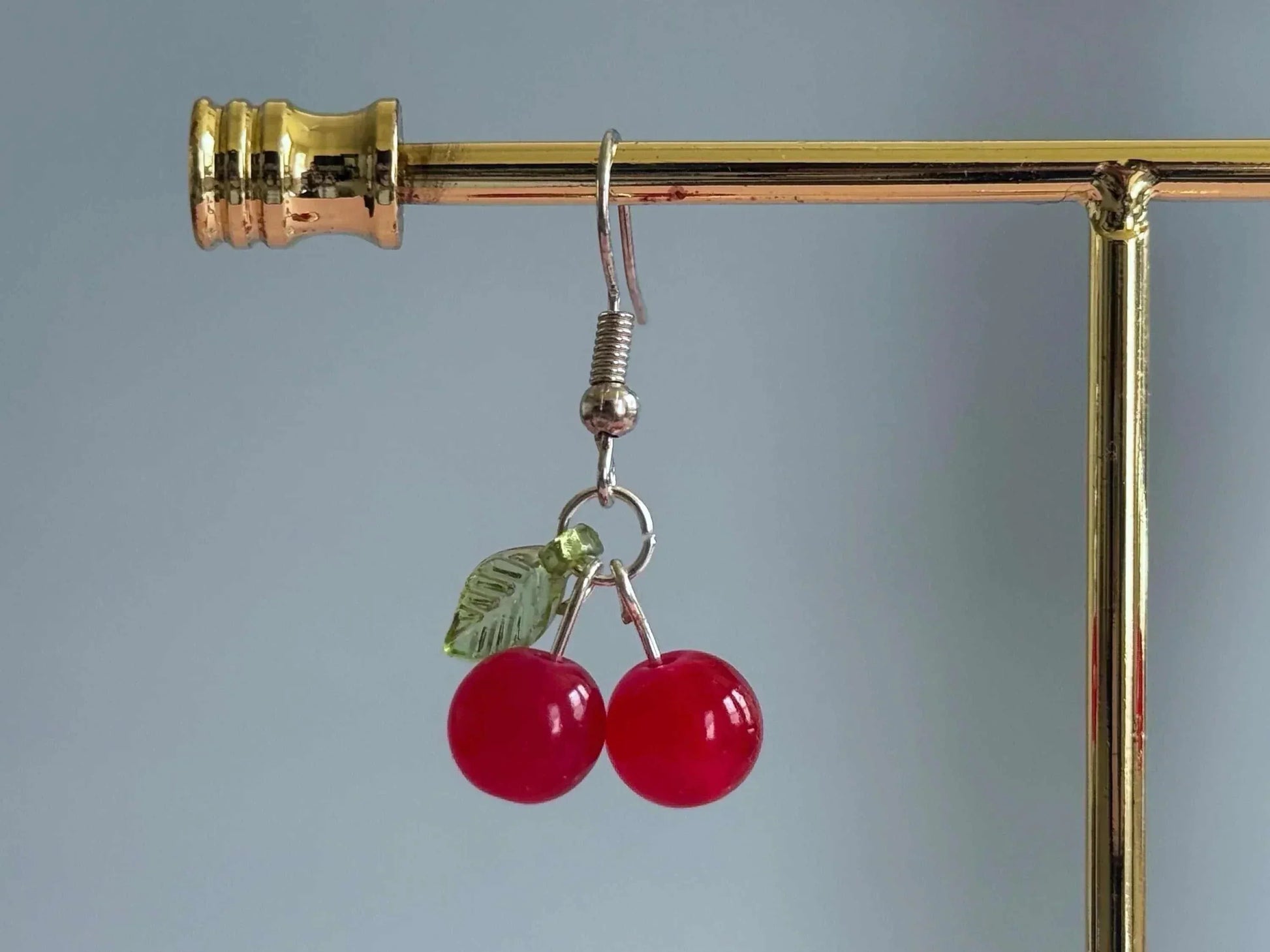 Handmade cherry dangle earrings with red glass beads and a green leaf, perfect for summer.