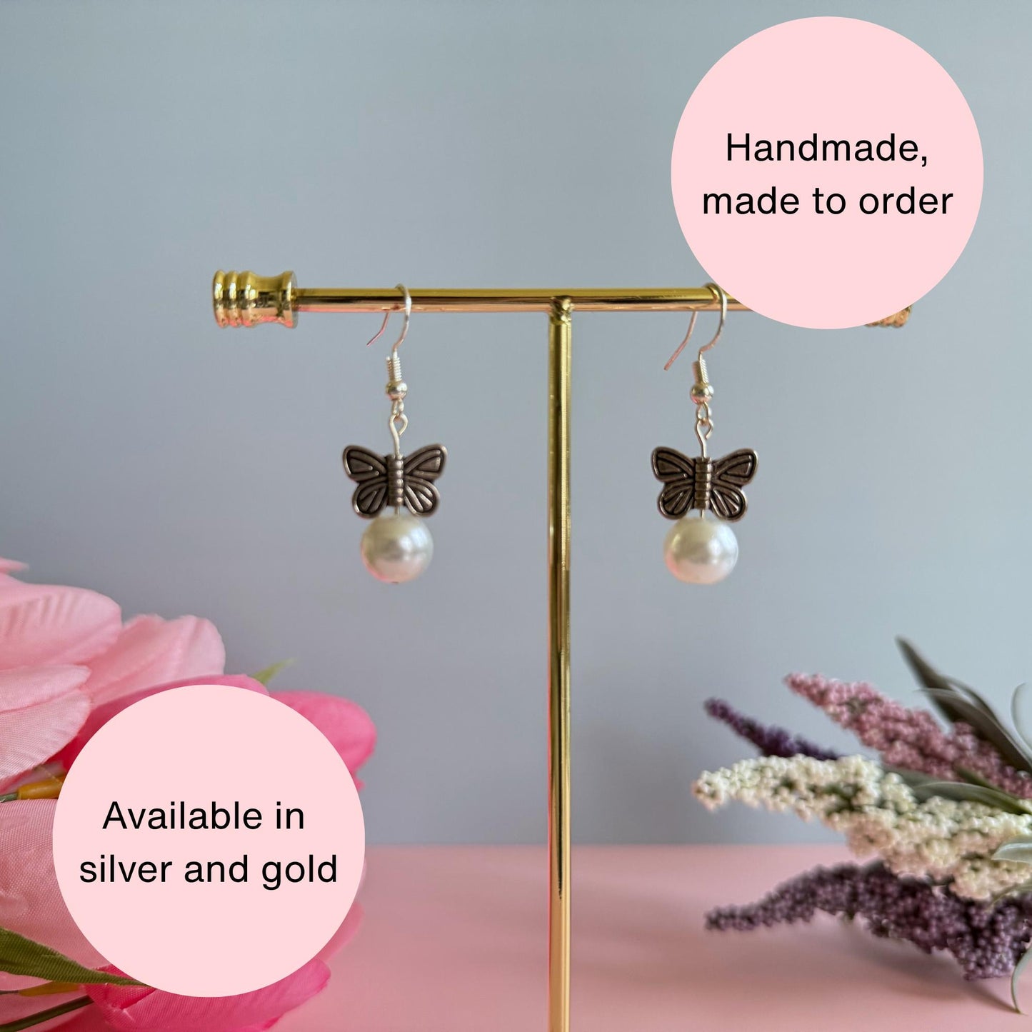 A pair of silver earrings butterfly earrings on a stand with flowers in the background. The photo also has text explaining that the earrings are handmade and made to order and available in gold or silver. The earrings feature metal butterflies and a pearl under the butterfly.