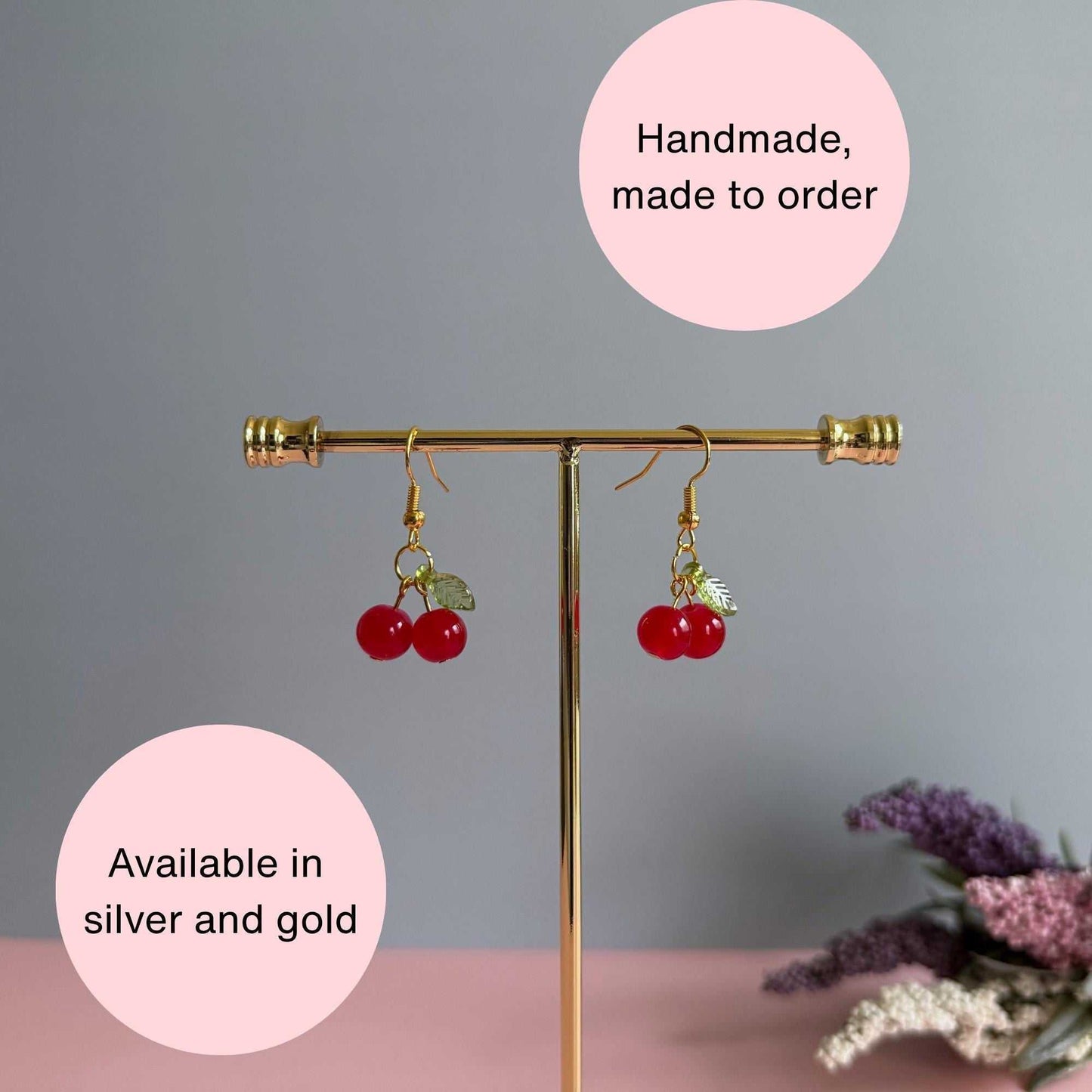 Red cherry earrings on a stand with text explaining that the earrings are in silver or gold and made to order