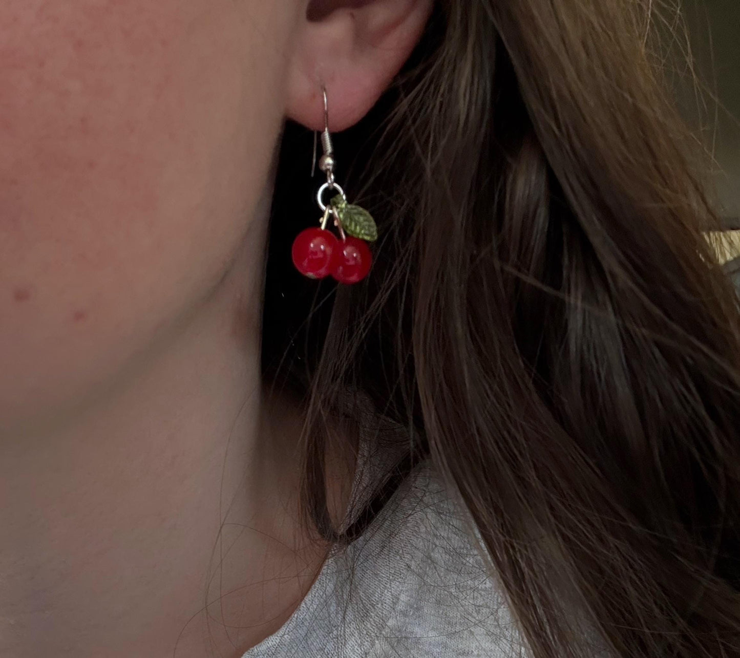 A pair of silver cherry earrings in ear.