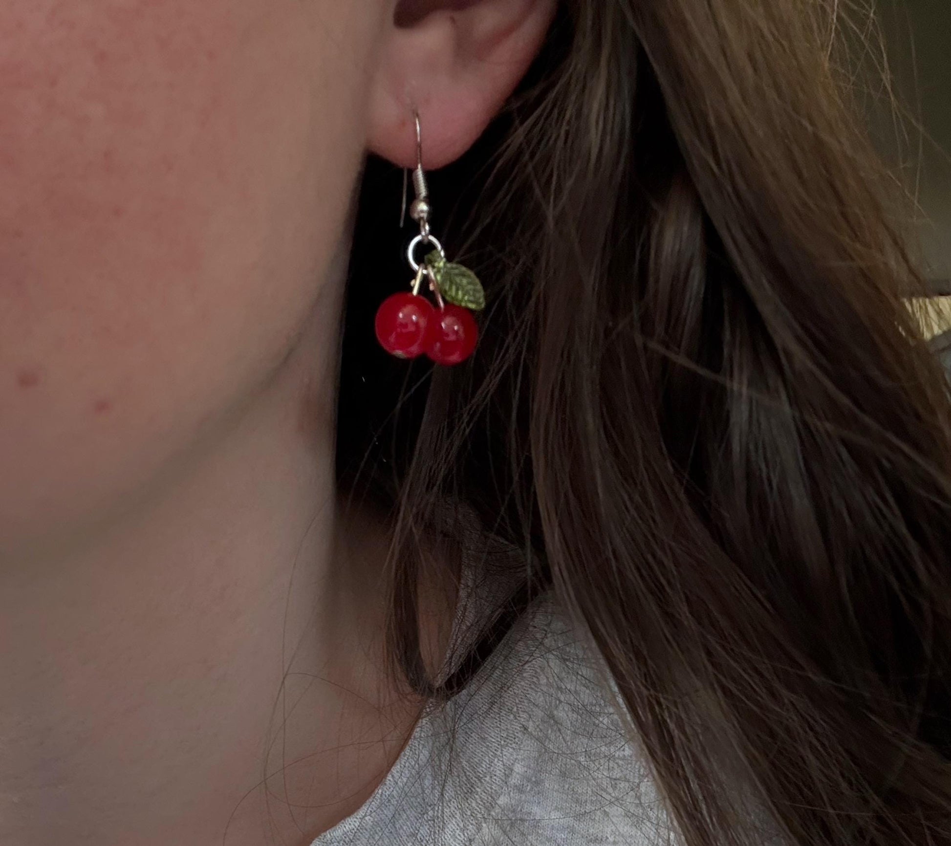 A pair of silver cherry earrings in ear.