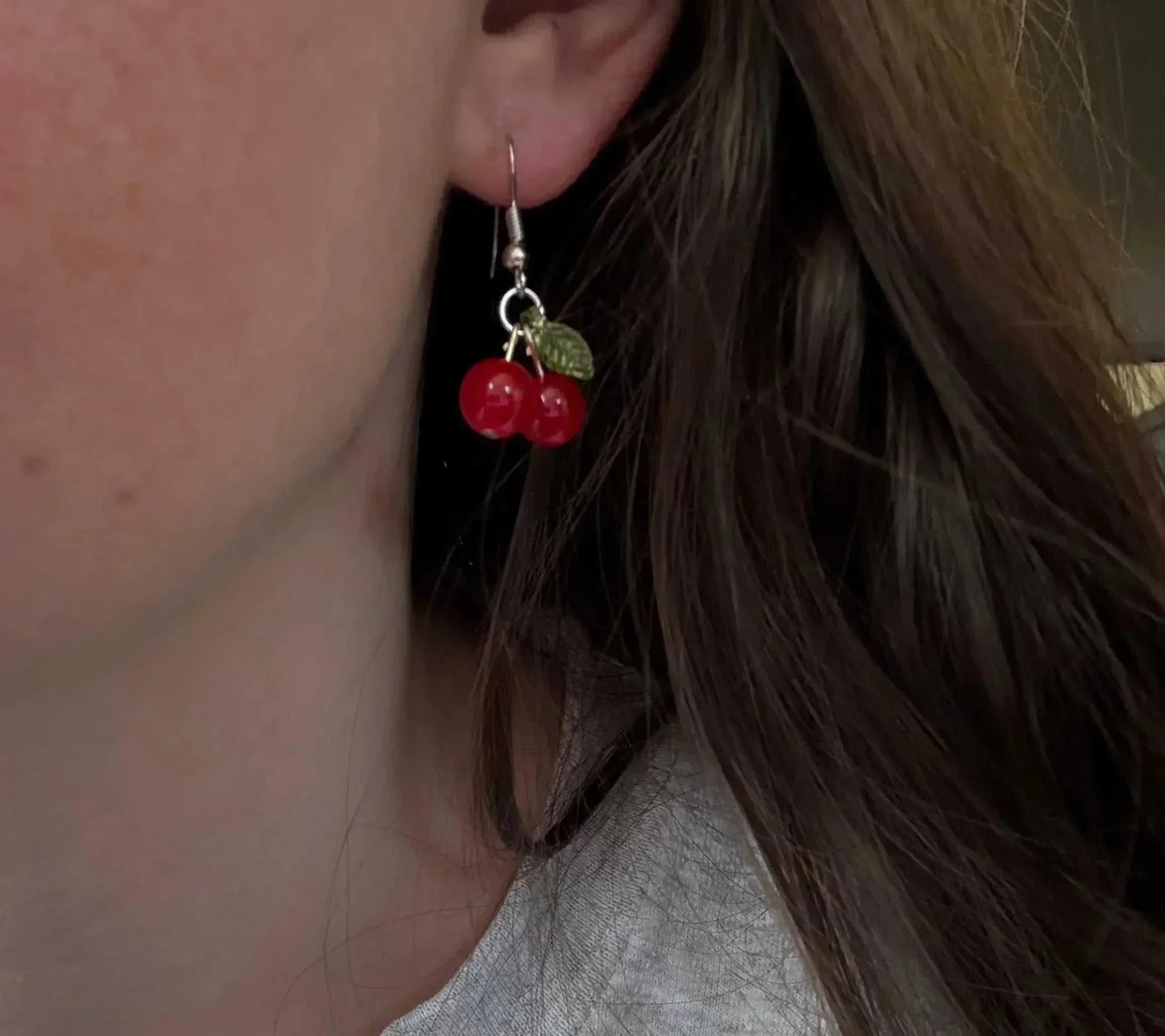 Red cherry earrings being worn in the ear lobe